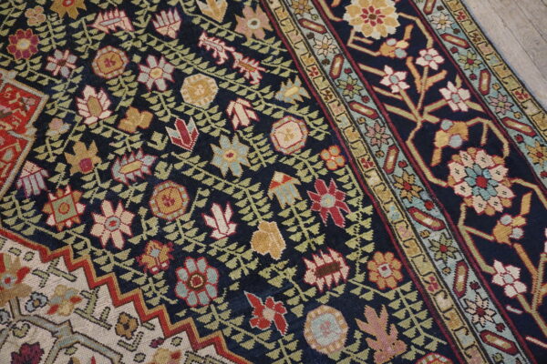 Intricate traditional rug with red, gold, and cream florals on a dark navy field, resting on gray wood.