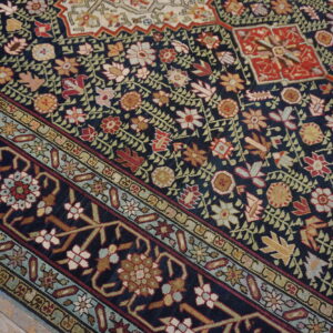 Intricate floral patterns in red, beige, and green stand out on a dark blue rug next to rustic wood floors.