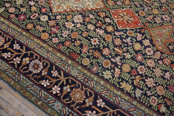 Intricate floral patterns in red, beige, and green stand out on a dark blue rug next to rustic wood floors.