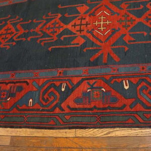 Traditional rug featuring bold red geometric patterns on a dark blue field, resting on hardwood floors.
