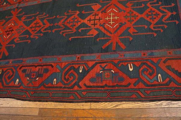 Traditional rug featuring bold red geometric patterns on a dark blue field, resting on hardwood floors.