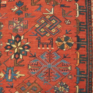 Red rug detail showing complex geometric motifs and stylized animal figures in blue, cream, and navy.