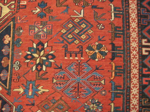 Red rug detail showing complex geometric motifs and stylized animal figures in blue, cream, and navy.