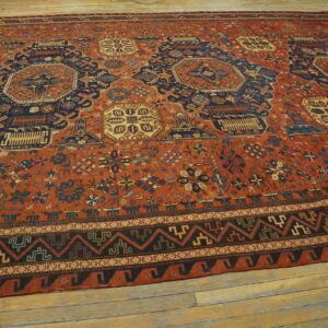 Terracotta and navy blue low-pile rug with complex geometric patterns covers distressed light wood flooring.