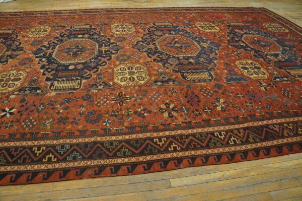 Terracotta and navy blue low-pile rug with complex geometric patterns covers distressed light wood flooring.