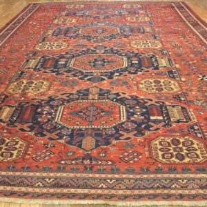 Long, traditional rug with a geometric pattern in rust, navy, and cream covers wood floorboards.