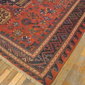 Red, blue, and black geometric rug corner placed on rustic light wood plank flooring.