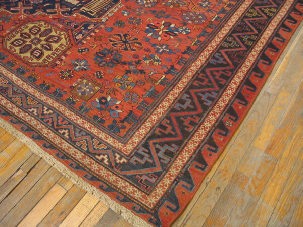 Red, blue, and black geometric rug corner placed on rustic light wood plank flooring.