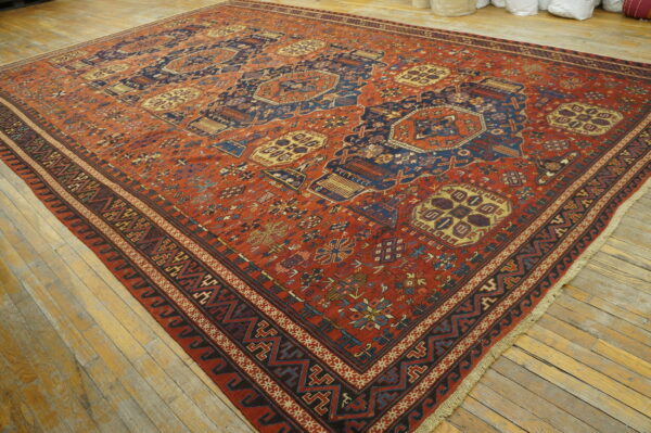 Large low-pile rug featuring red, indigo, and cream geometric tribal motifs on distressed light wooden floors.