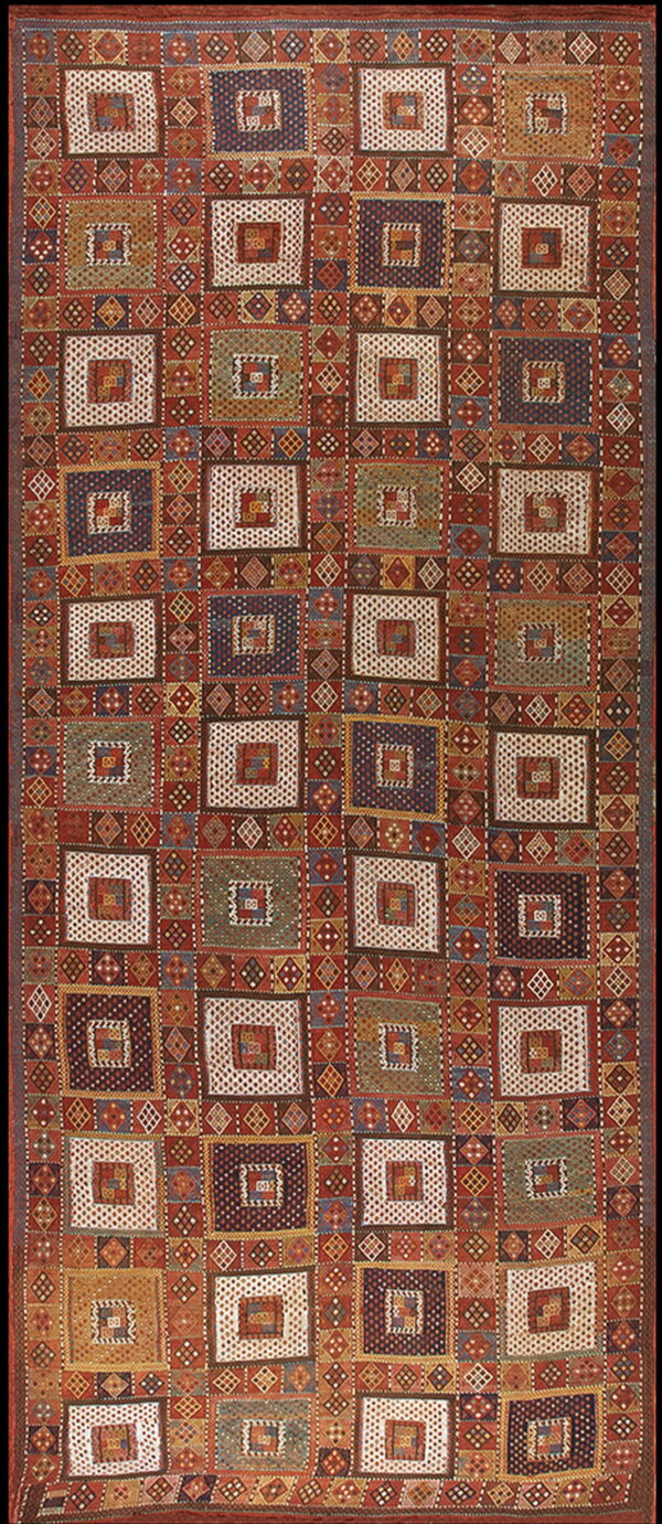 Geometric rug displaying block patterns of nested squares in shades of rust, blue, cream, and green.