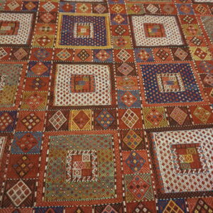Detailed flatwoven rug with a geometric patchwork pattern featuring nested squares in red, white, blue, and gold.
