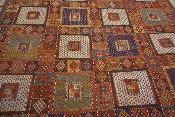 Detailed flatwoven rug with a geometric patchwork pattern featuring nested squares in red, white, blue, and gold.