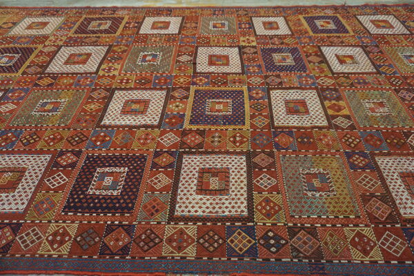 Rust and multicolor geometric flatweave rug featuring large squares filled with intricate patterns.