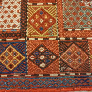 Geometric flatweave detail showing complex diamonds and lattice patterns in rust, blue, yellow, and cream.