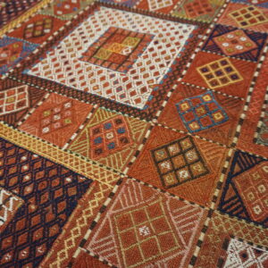 Close-up of a geometric rug with diamond and square patterns in rust, navy, gold, and white.