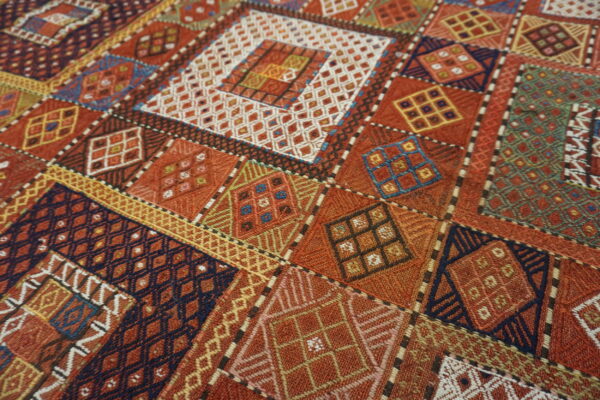 Close-up of a geometric rug with diamond and square patterns in rust, navy, gold, and white.