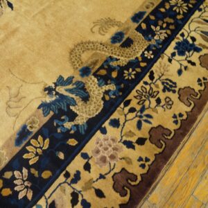 Tan field rug with blue and brown traditional dragon and floral border on distressed yellow wood floor.
