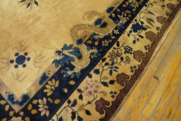Tan field rug with blue and brown traditional dragon and floral border on distressed yellow wood floor.