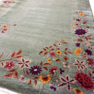 Soft sage green rug with a dense border of colorful floral motifs in purple, gold, and red.