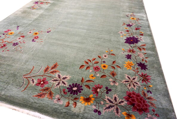 Soft sage green rug with a dense border of colorful floral motifs in purple, gold, and red.