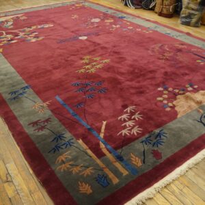 High-pile red rug with multicolored floral and scenic patterns, bordered in gray, lying on wood floors.