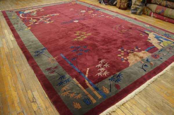 High-pile red rug with multicolored floral and scenic patterns, bordered in gray, lying on wood floors.
