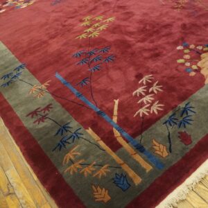 Angled view of a deep red rug with a grey border and colorful bamboo patterns on worn wood floors.
