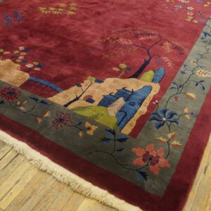 Burgundy rug featuring a pictorial landscape pattern and a wide gray floral border rests on wood flooring.