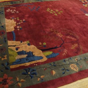 Deep red rug with a detailed naturalistic pattern and wide grey-green floral border on wood floors.