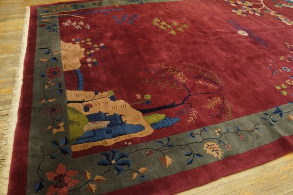 Deep red rug with a detailed naturalistic pattern and wide grey-green floral border on wood floors.