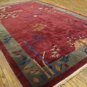Deep red rug featuring stylized bamboo and blossoms, bordered in grey-green, resting on light wood flooring.