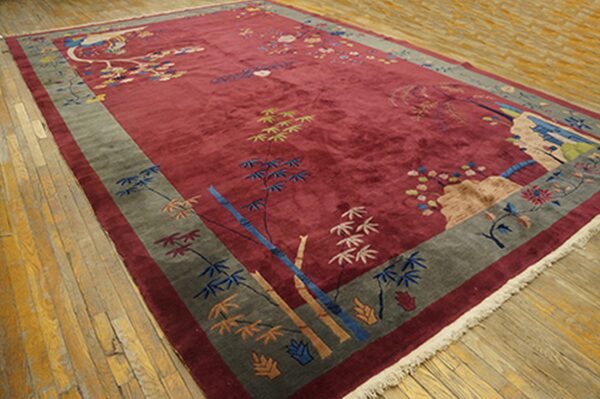 Deep red rug featuring stylized bamboo and blossoms, bordered in grey-green, resting on light wood flooring.