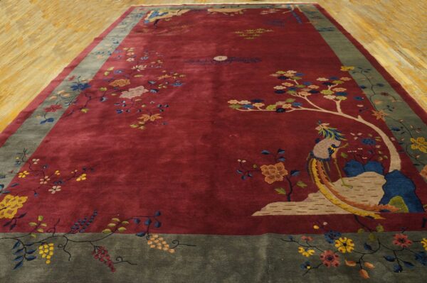 A large maroon rug with a figural bird and detailed floral border rests on light wood floors.
