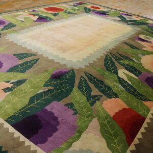 Colorful rug with cream scalloped center, large purple flowers, green leaves, and a zigzag border on wood flooring.
