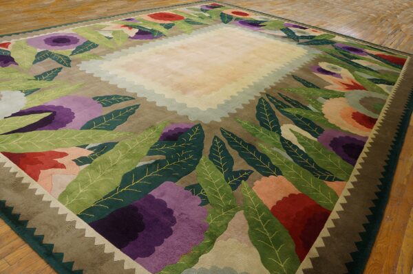 Colorful rug with cream scalloped center, large purple flowers, green leaves, and a zigzag border on wood flooring.