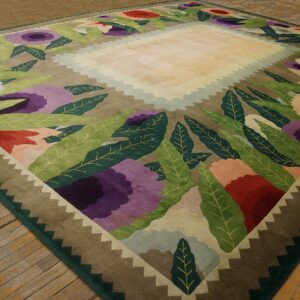 Olive and purple floral rug with stylized leaves and a zigzag border on distressed wood floors.