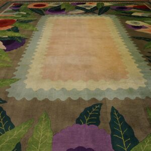 Oversized rug with a bold, colorful floral border surrounding a light peach scalloped central field on wood flooring.