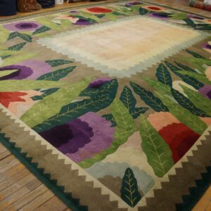 A large rug with stylized purple, red, and green flowers surrounds a pale yellow central field on a wood floor.