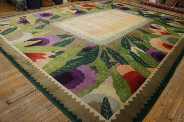 A large rug with stylized purple, red, and green flowers surrounds a pale yellow central field on a wood floor.
