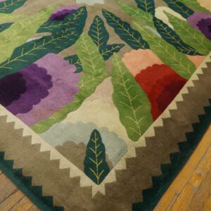 A multicolored floral rug with a carved pile and stepped border rests on distressed wood plank flooring.