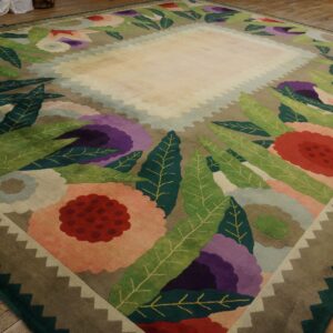 Sculpted rug featuring large purple, red, and green stylized flowers bordering a solid light-colored field.