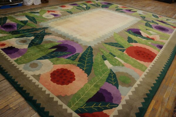 Sculpted rug featuring large purple, red, and green stylized flowers bordering a solid light-colored field.
