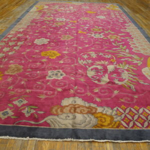 Bright pink rug featuring detailed floral vines, cloud motifs, and a wide dark border on hardwood flooring.