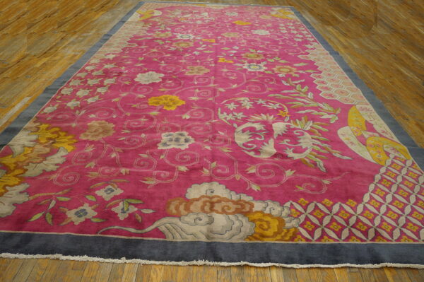 Bright pink rug featuring detailed floral vines, cloud motifs, and a wide dark border on hardwood flooring.