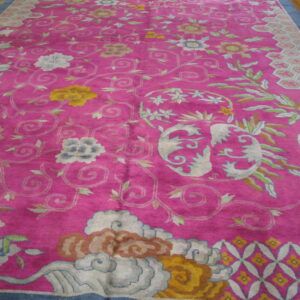 Bright pink rug with light blue, yellow, and cream scrolling floral and cloud motifs on a wood floor.