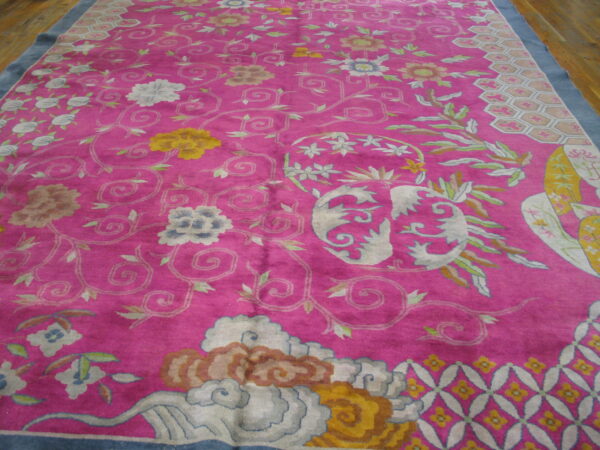 Bright pink rug with light blue, yellow, and cream scrolling floral and cloud motifs on a wood floor.