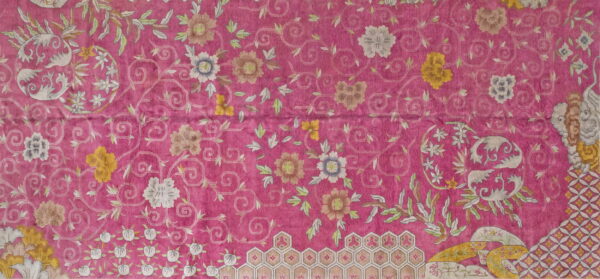 Detail of a vivid magenta rug patterned with scrolling foliage, pale flowers, and honeycomb borders.