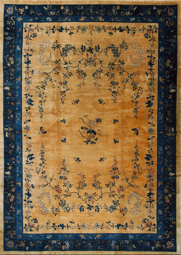 Gold rug featuring sprawling blue and pink floral vines, birds, and a wide dark blue patterned border.