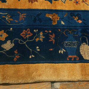 Close-up showing a dense-pile rug with indigo floral vines and ceramic motifs bordered by thick mustard yellow bands.