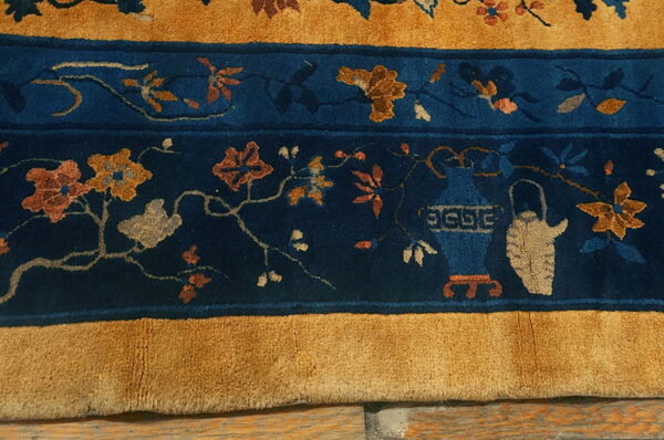 Close-up showing a dense-pile rug with indigo floral vines and ceramic motifs bordered by thick mustard yellow bands.